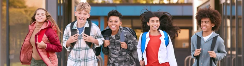Five school children with backpacks outside a school building