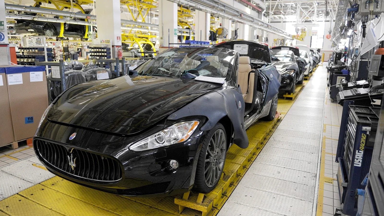 Black Maserati sports cars on an automotive assembly line inside a brightly lit factory