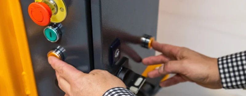 Close-up of hands operating the two-hand control buttons on a Bramidan baler, highlighting safety standards