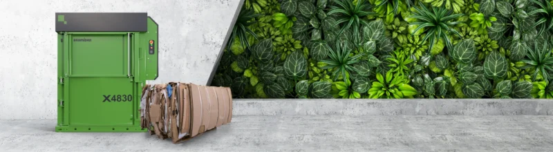 Green X4830 baler with cardboard in front placed on concrete with green plants